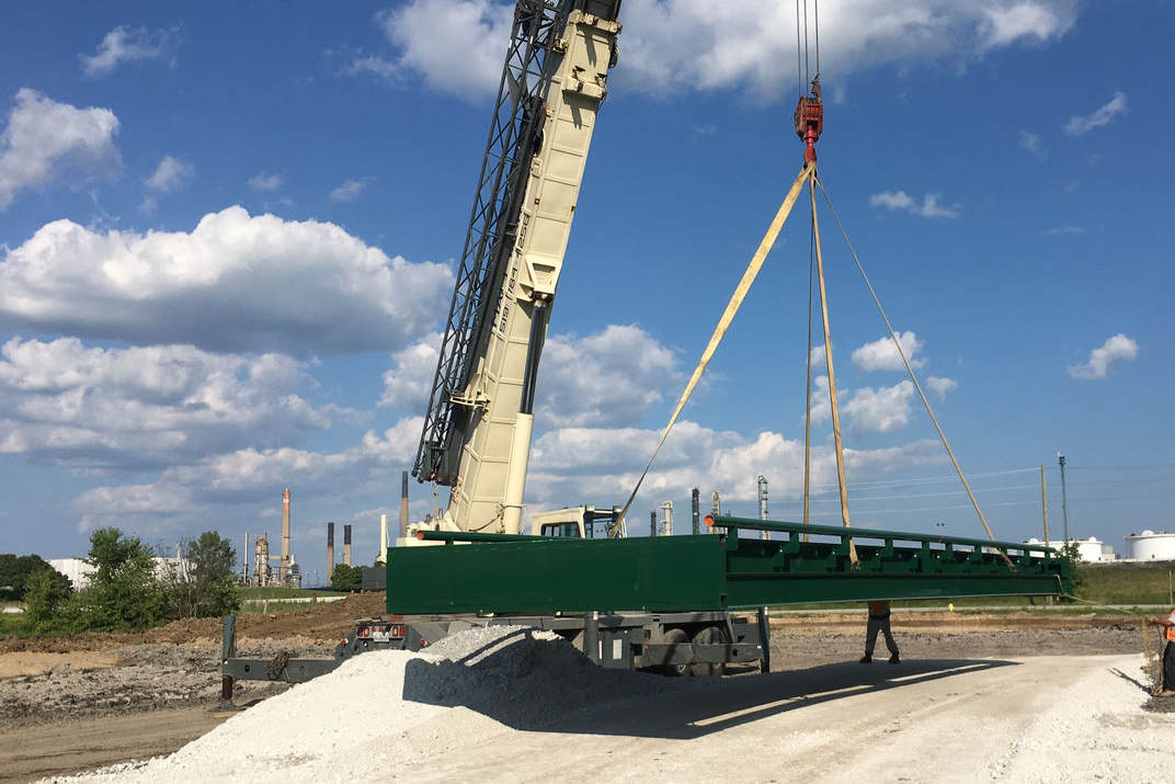 A green Ramara portable heavy capacity vehicle weighing scale is being lowered with a crane.